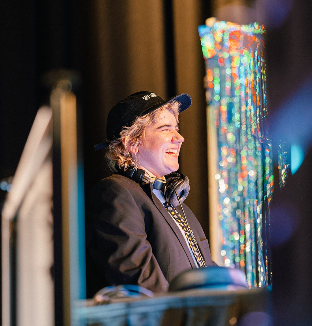 A DJ in a cap and headphones laughing at the decks