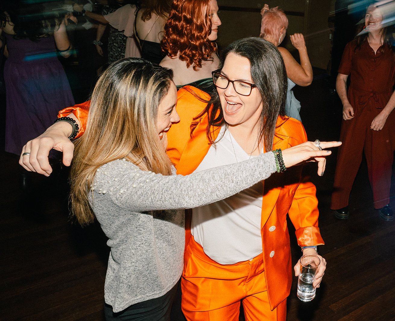 Two guests laughing and dancing together, one in a bright orange suit