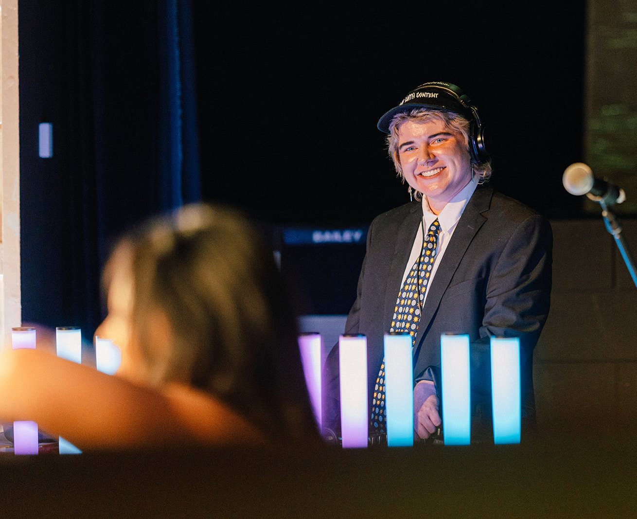 A DJ in a suit and headphones smiling behind the decks