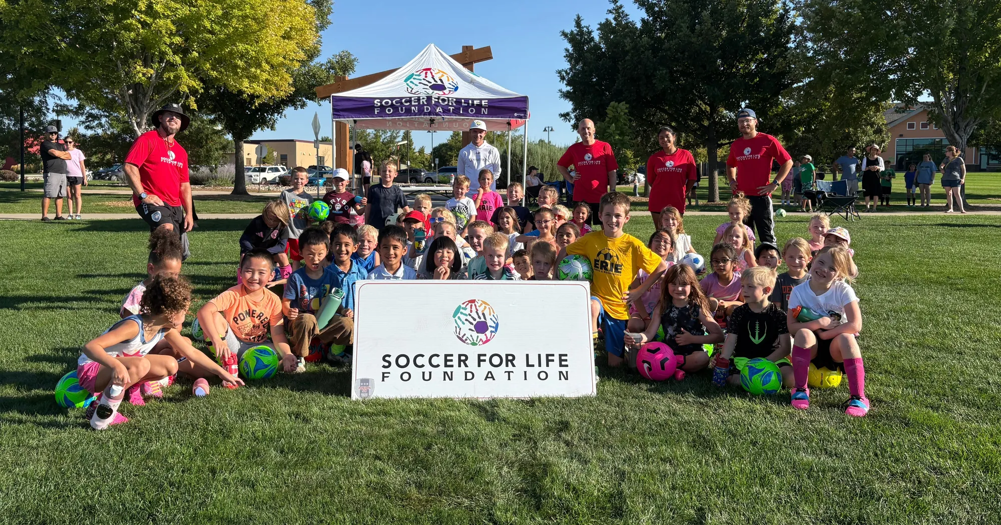 Kids and Soccer for Life Foundation coaches gathered around the foundation's banner at a community soccer event