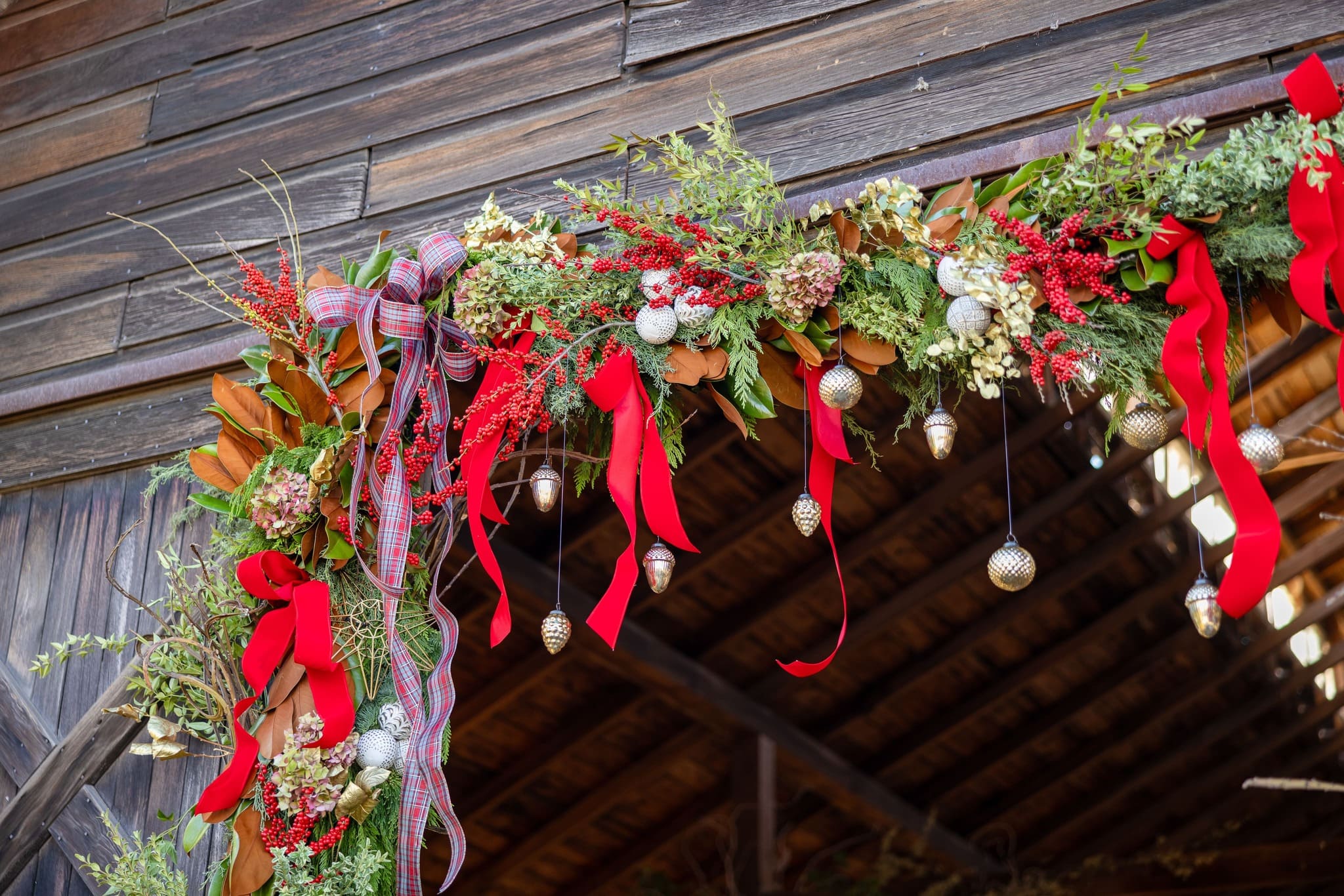 Holiday barn garland installation with evergreens, red ribbon, and seasonal accents.
