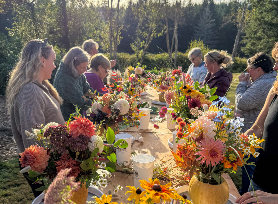 Guests arranging fall flowers and greenery in pumpkins at a long outdoor table at Turnbull Farm.
