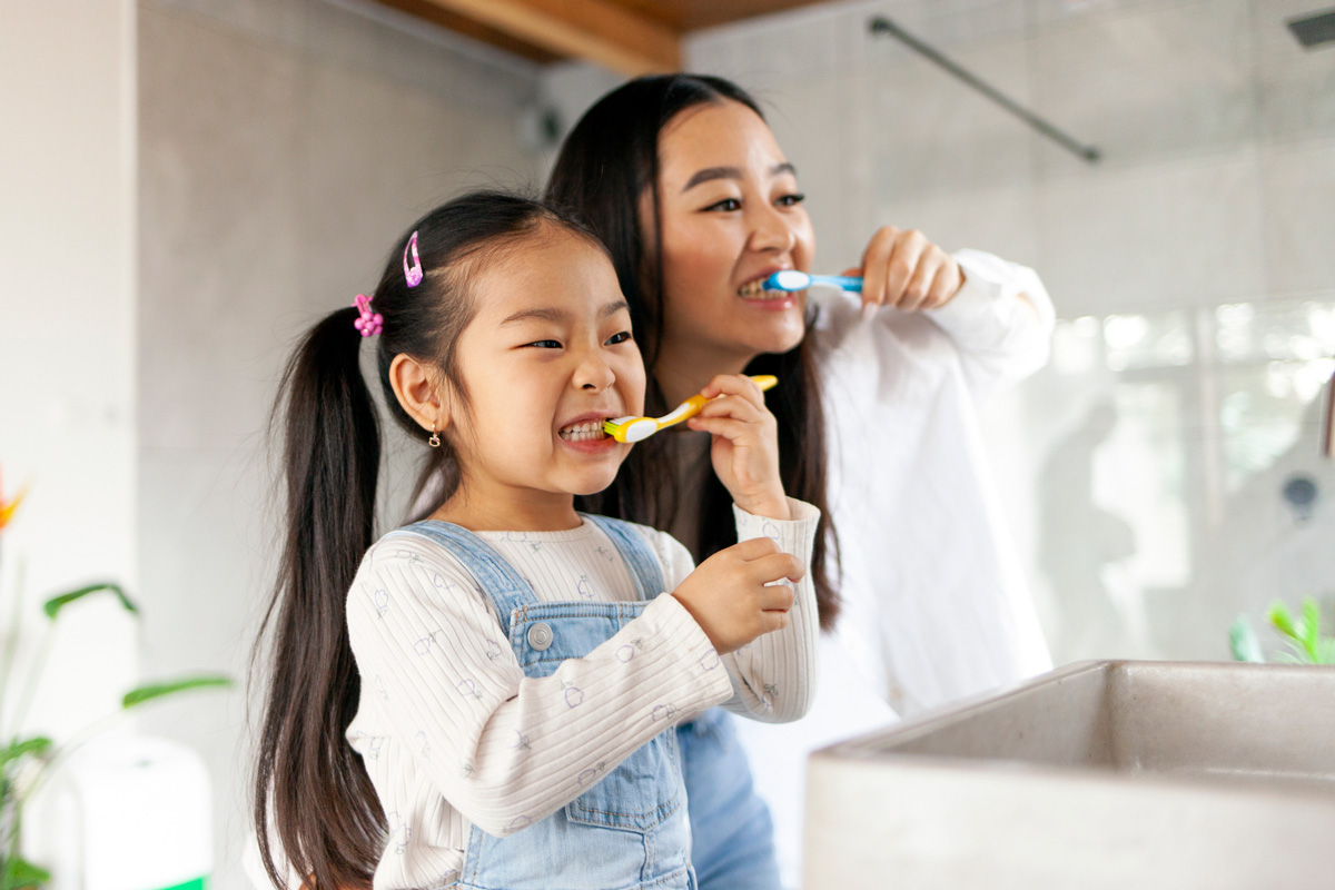 A mother and daughter practice good oral hygiene habits by brushing their teeth together after a meal.