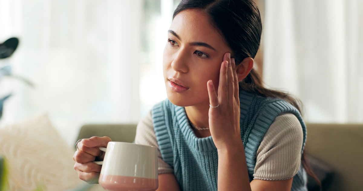 A woman drinking coffee grabs her head in pain.