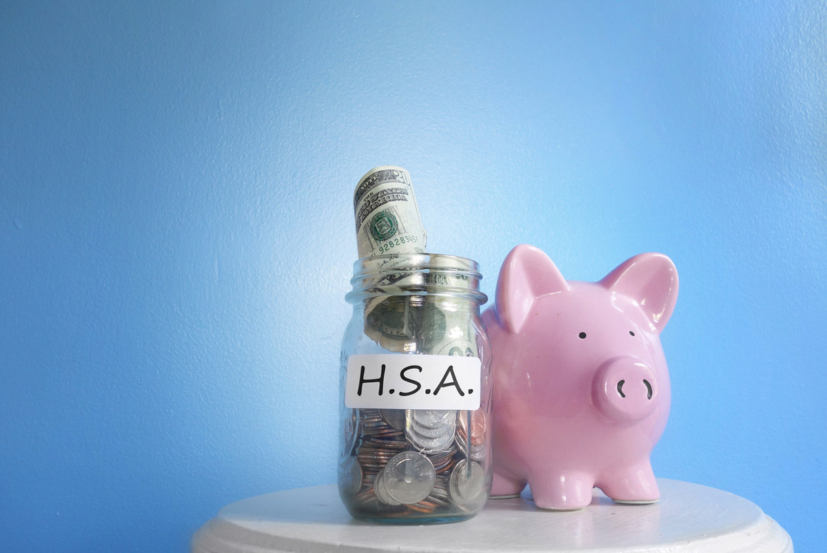 A piggy bank sits next to a jar of money labeled "HSA".