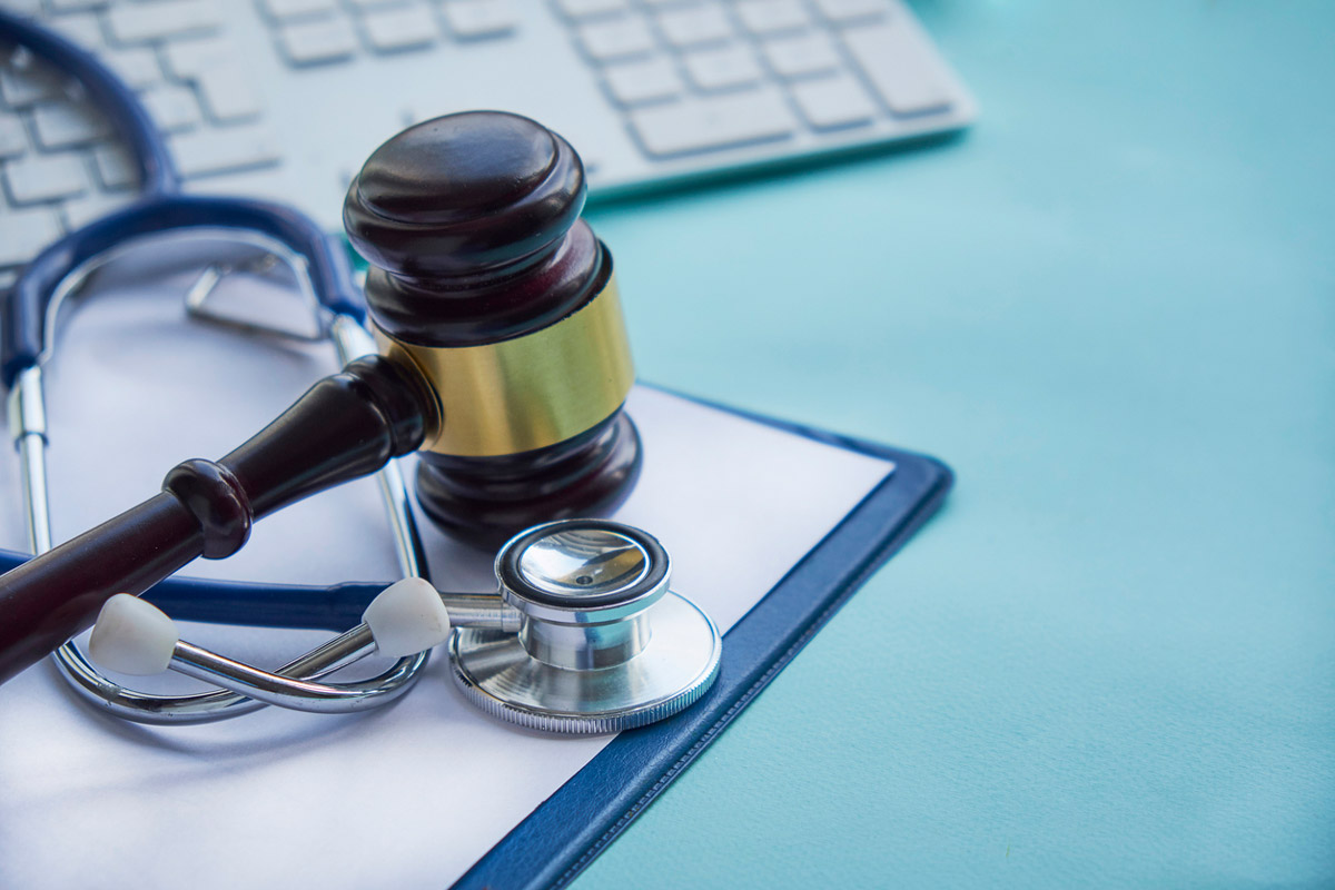 A clipboard with medical forms sits on a blue background next to a stethoscope and a judge's gavel.