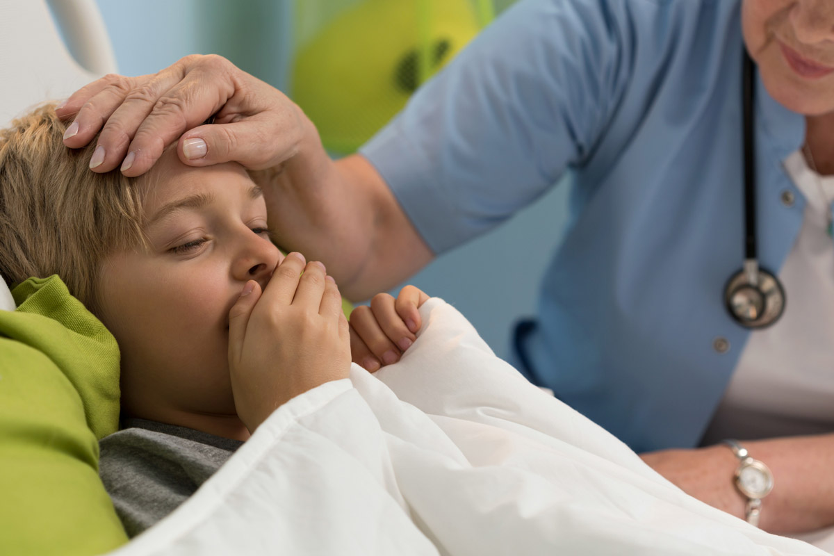 A young boy coughs while sick in bed.