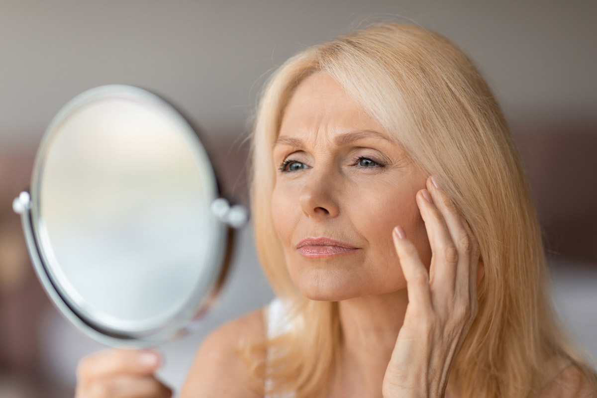 A woman looks at the wrinkles on her skin in the mirror.
