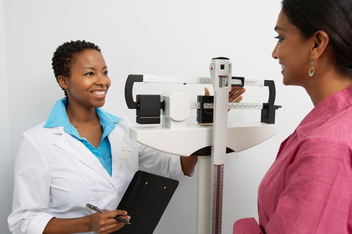 A doctor weighs a patient at their office.