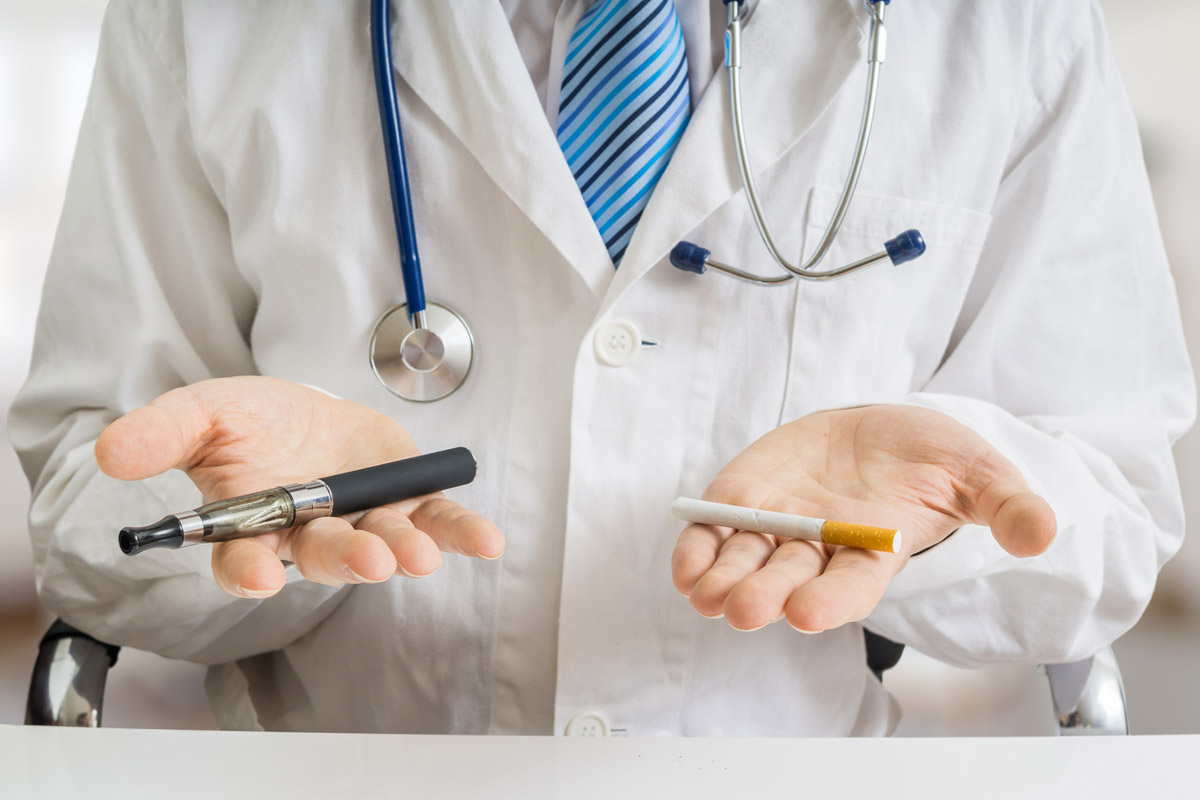 A doctor holds a cigarette and vape in each of his hands.