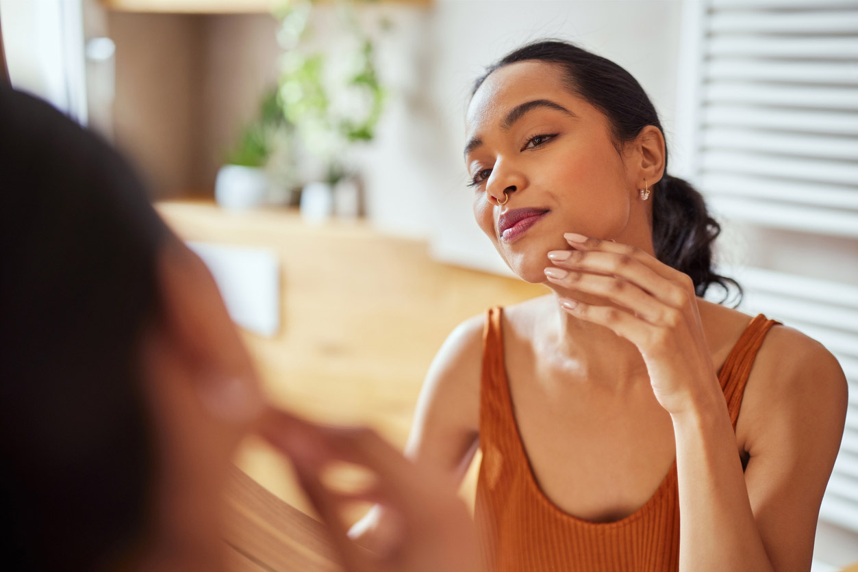 A woman looks at her skin in the mirror to determine her skin type.