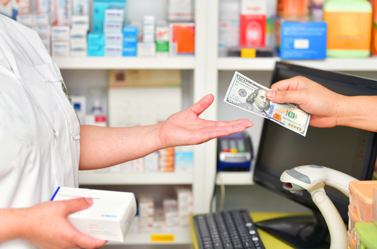 A pharmacy owner is handed money at the checkout counter. 
