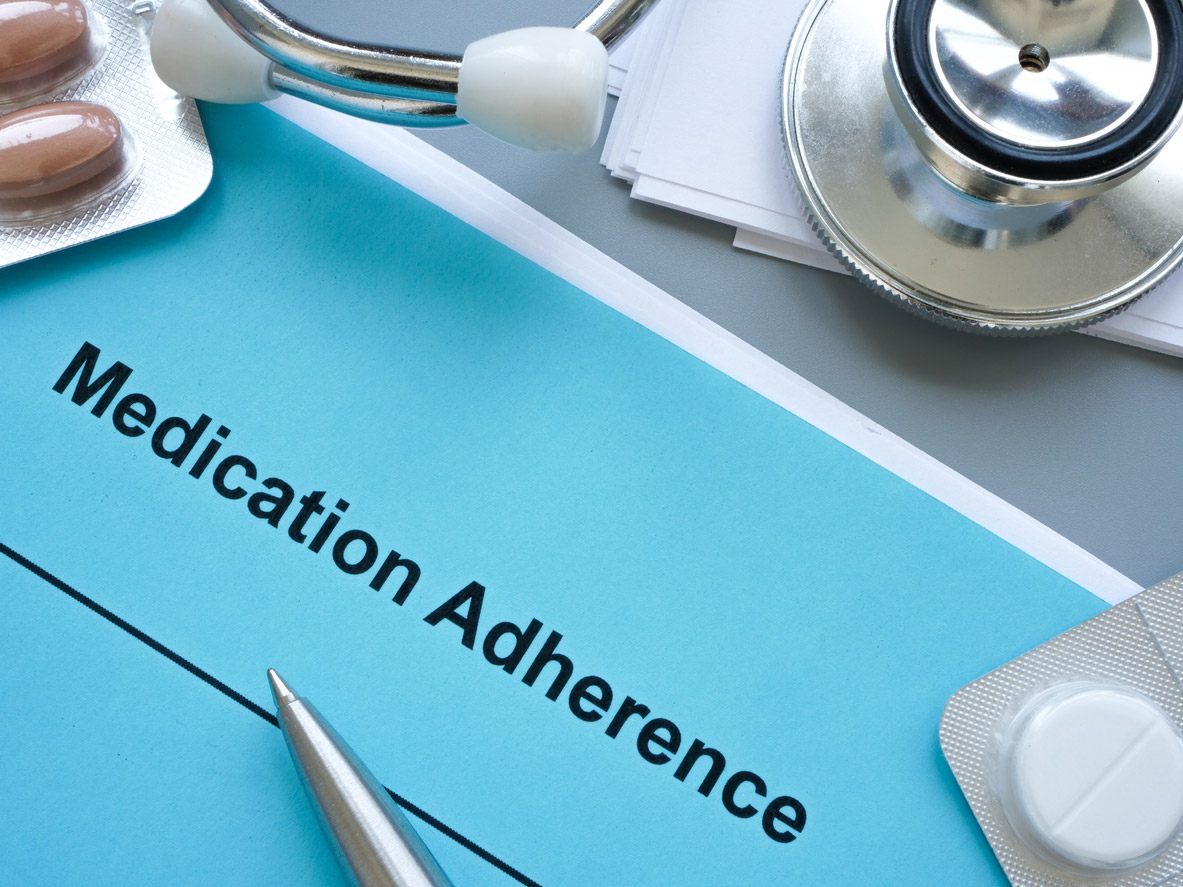 A paper reads medication adherence and is surrounded by medicine and a stethoscope. 
