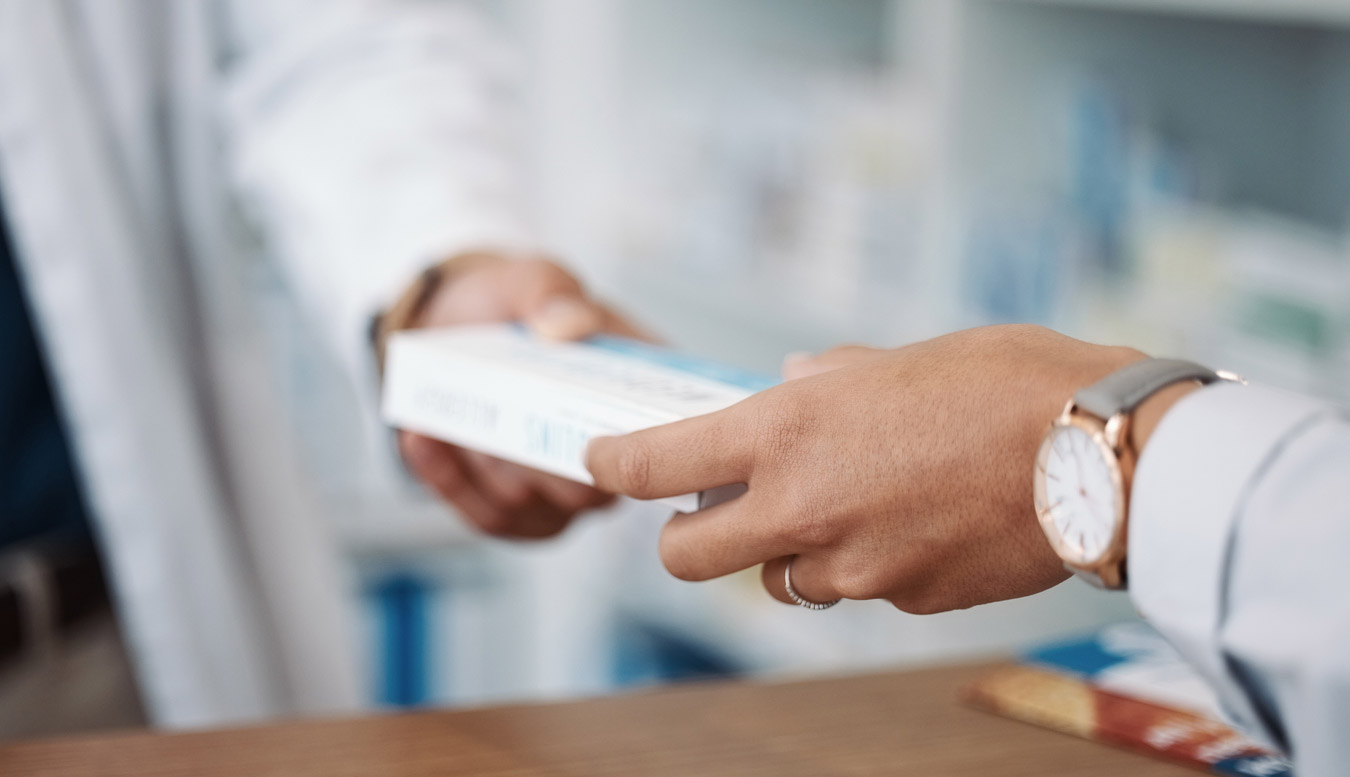 A pharmacist passes over a prescription to a patient.