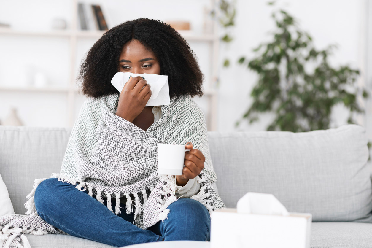 A woman with the flu drinks a warm drink to soothe her sore throat. 