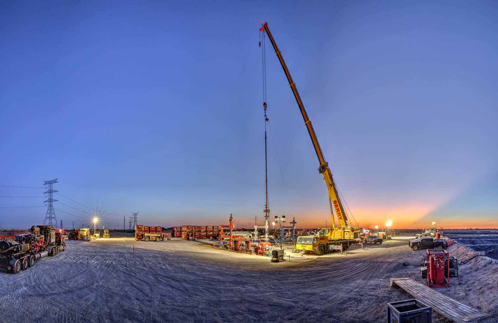 Nighttime photo of a well site, including a crane, vehicles, and drilling equipment