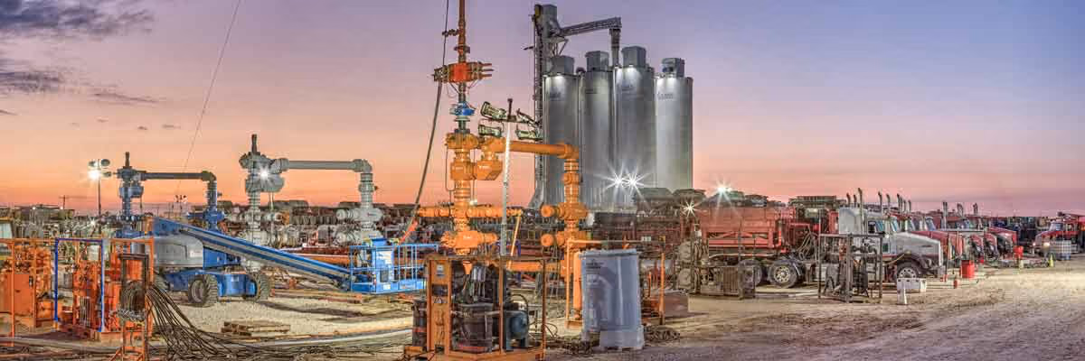 Nighttime photo of wellsite with vehicles, heavy machinery, and completions equipment visible