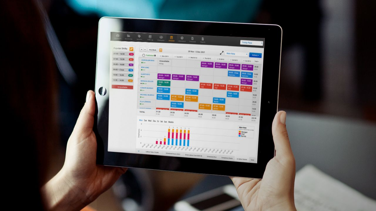 Une personne consultant le planning de son personnel sur une tablette avec la répartition des rôles en bas de l’écran.