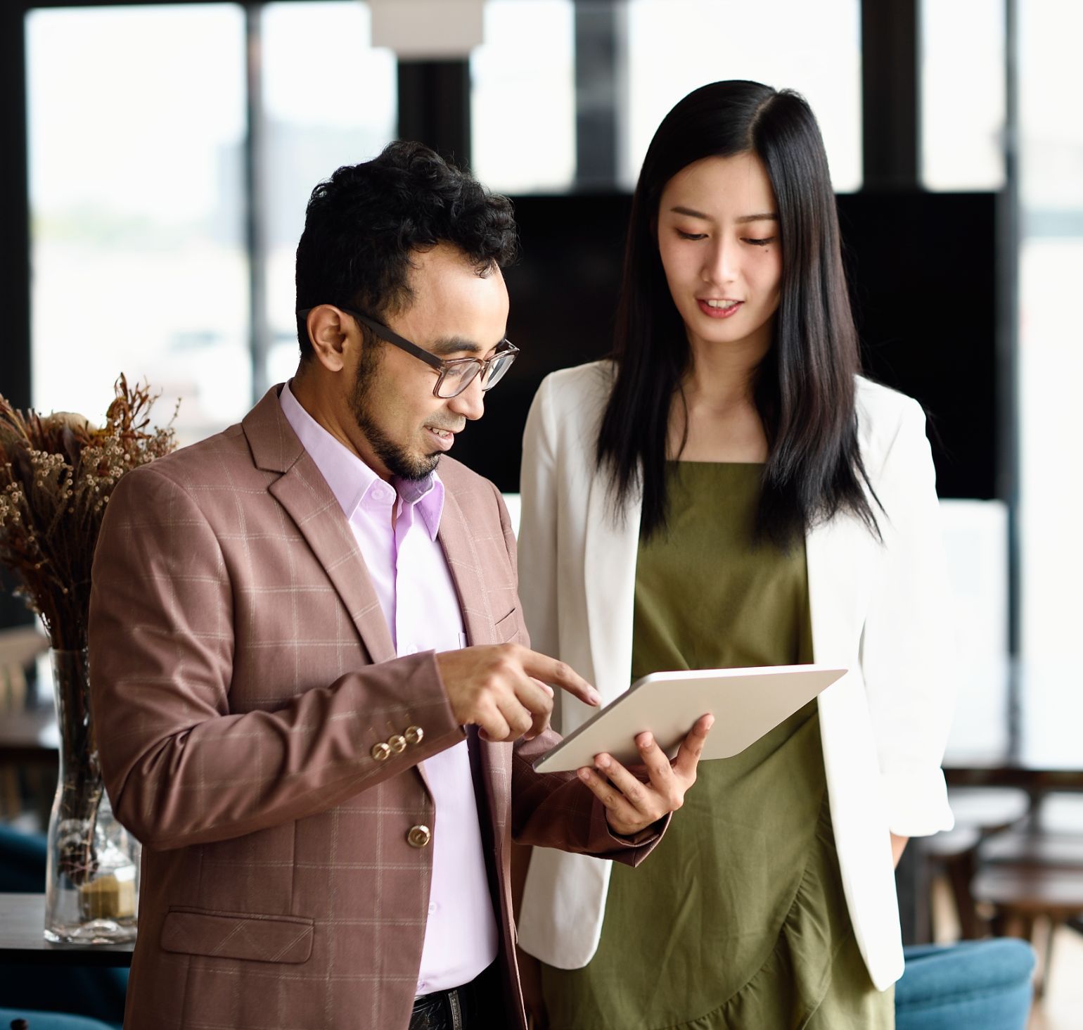 Image of a male and female collegues working together from the same tablet in an office setting.