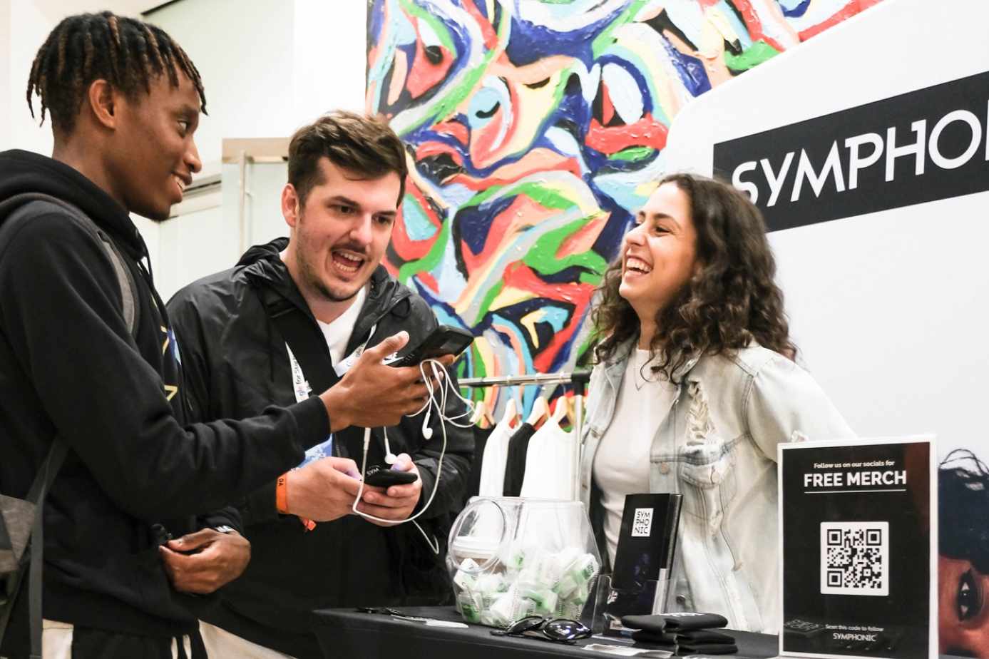 Three people gather happily around a Symphonic informational booth.