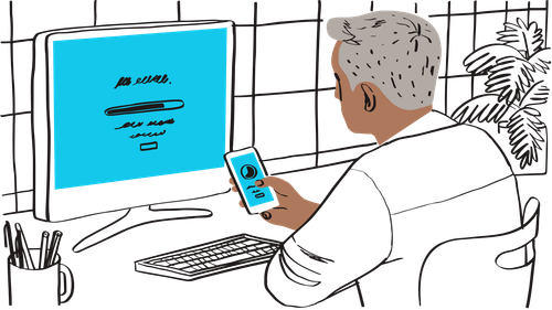 Individual using a smartphone, sitting at a desk with a computer screen in front.