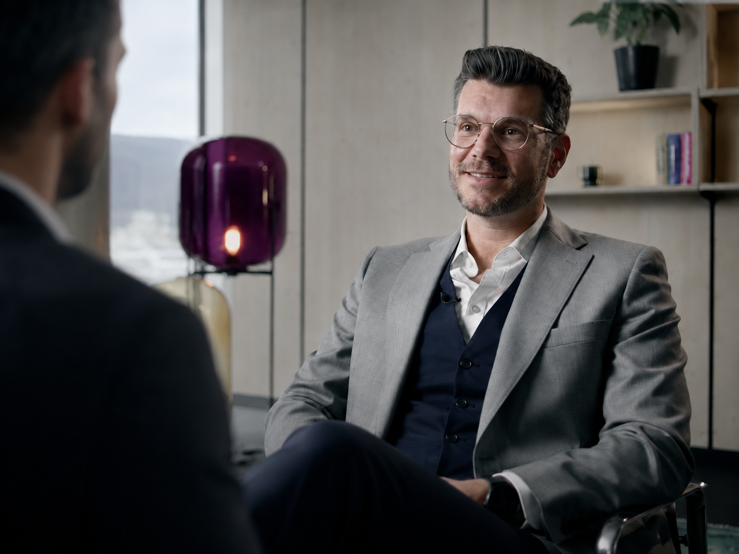 Mann im grauen Anzug und Brille führt entspanntes Gespräch in modernem Büro.