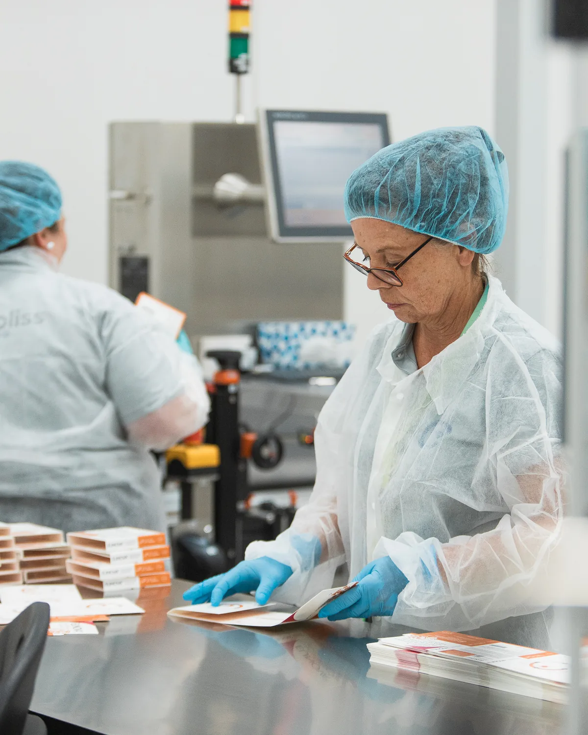 Operators in hairnets and gloves sorting printed cartons at a steel table by a packaging line