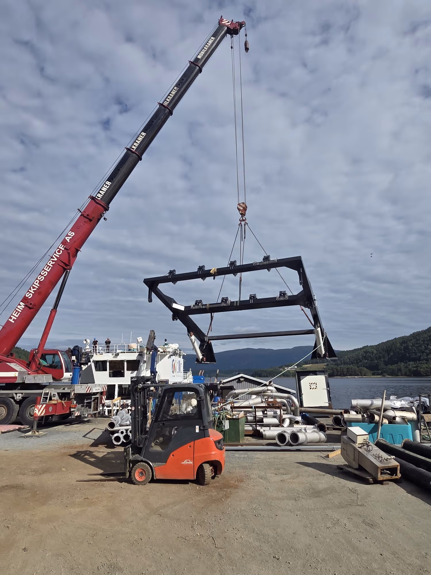 Stor mobilkran løfter A-rammen før installasjon på brønnbåten Selma ved verftsområdet ved sjøen.