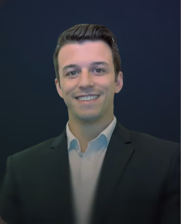 Portrait of a smiling young man with dark slicked-back hair wearing a white collared shirt and dark blazer against a dark gradient background.