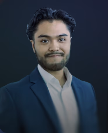 Young man with dark hair and beard wearing a white shirt and dark blazer, against a dark gradient background.