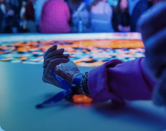 Close-up of a hand with a blue wristband reaching toward a table with many colorful poker chips, blurred people in the background.
