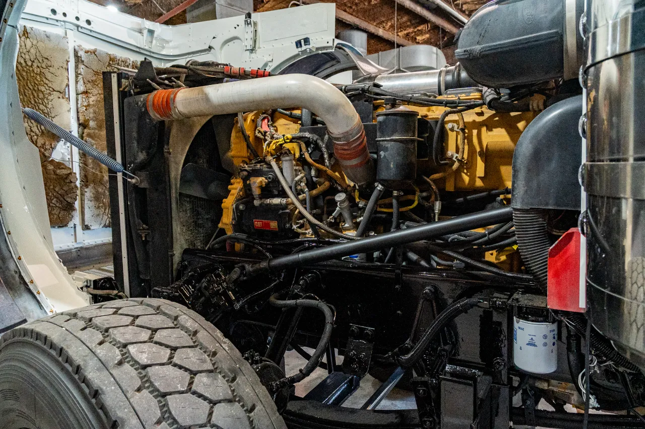 Exposed heavy-duty engine with visible CAT components and intake piping during truck repair in a service bay.