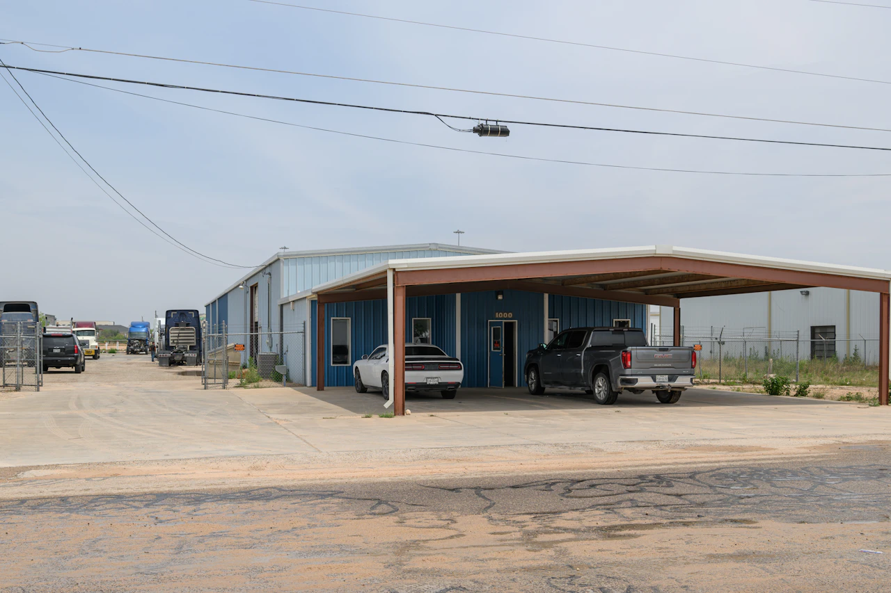 Roadside assistance service location with trucks and service vehicles parked outside blue repair facility with covered parking area and fenced truck yard.