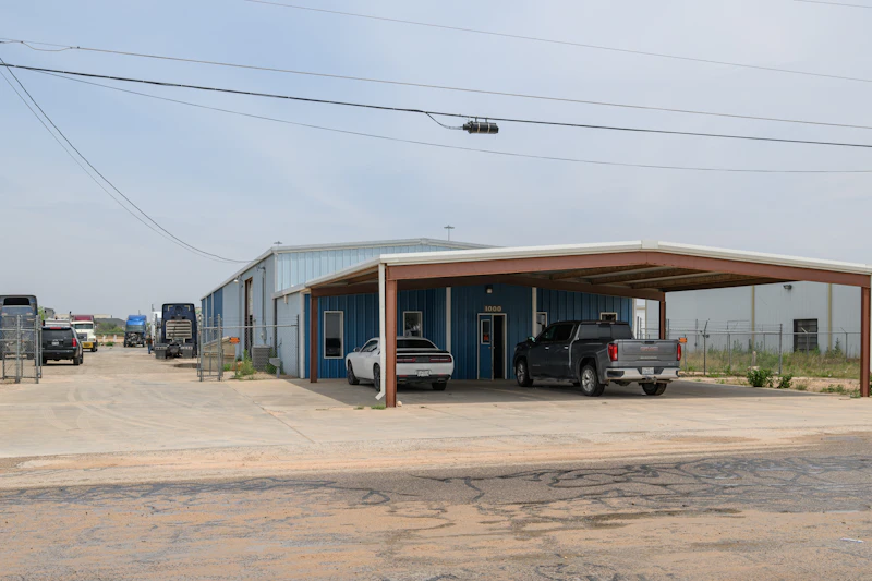 Roadside assistance service location with trucks and service vehicles parked outside blue repair facility with covered parking area and fenced truck yard.