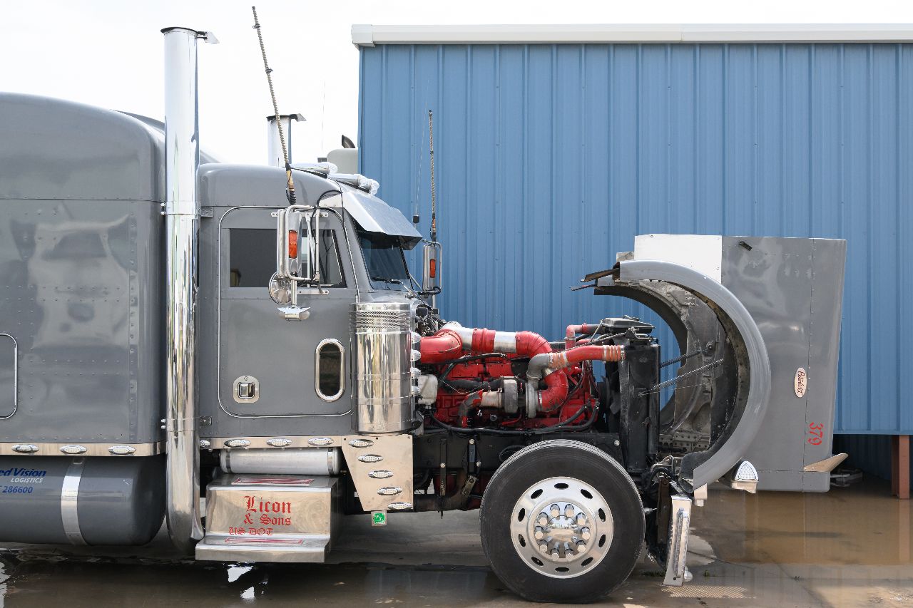 Semi truck idling with hood open during engine service outside repair shop.