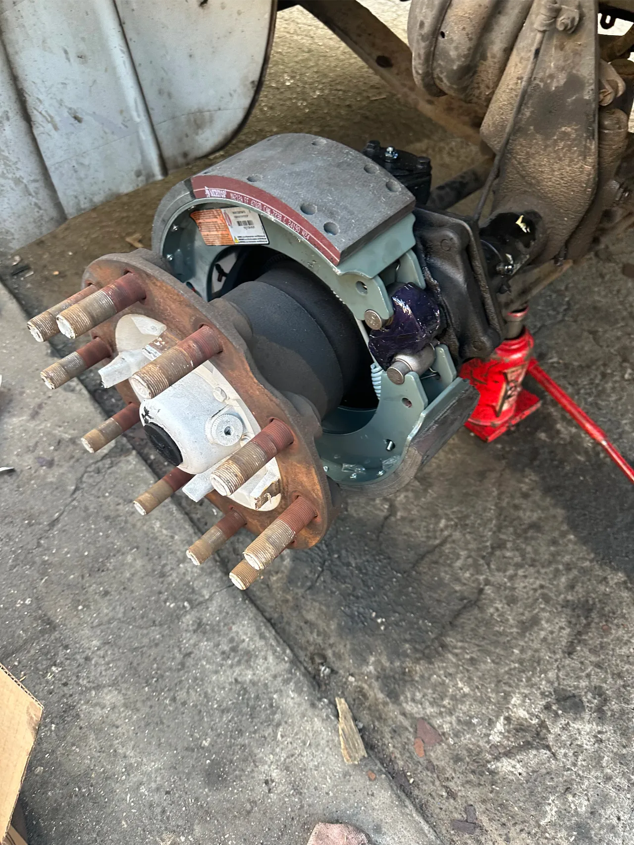 Brake shoe installation on a heavy-duty truck axle with hub exposed and new brake lining in place.
