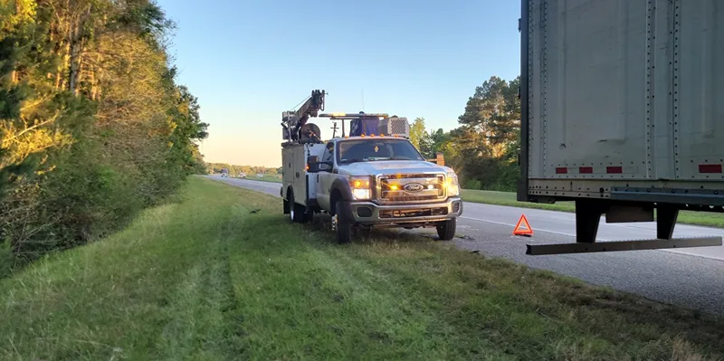 Breakdown in West Texas with a service truck assisting a disabled semi on the highway shoulder with a safety triangle.