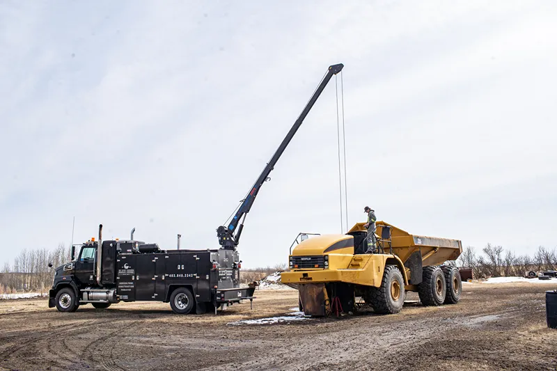 Towing service truck uses a boom beside a CAT articulated dump truck during heavy-duty roadside repair.