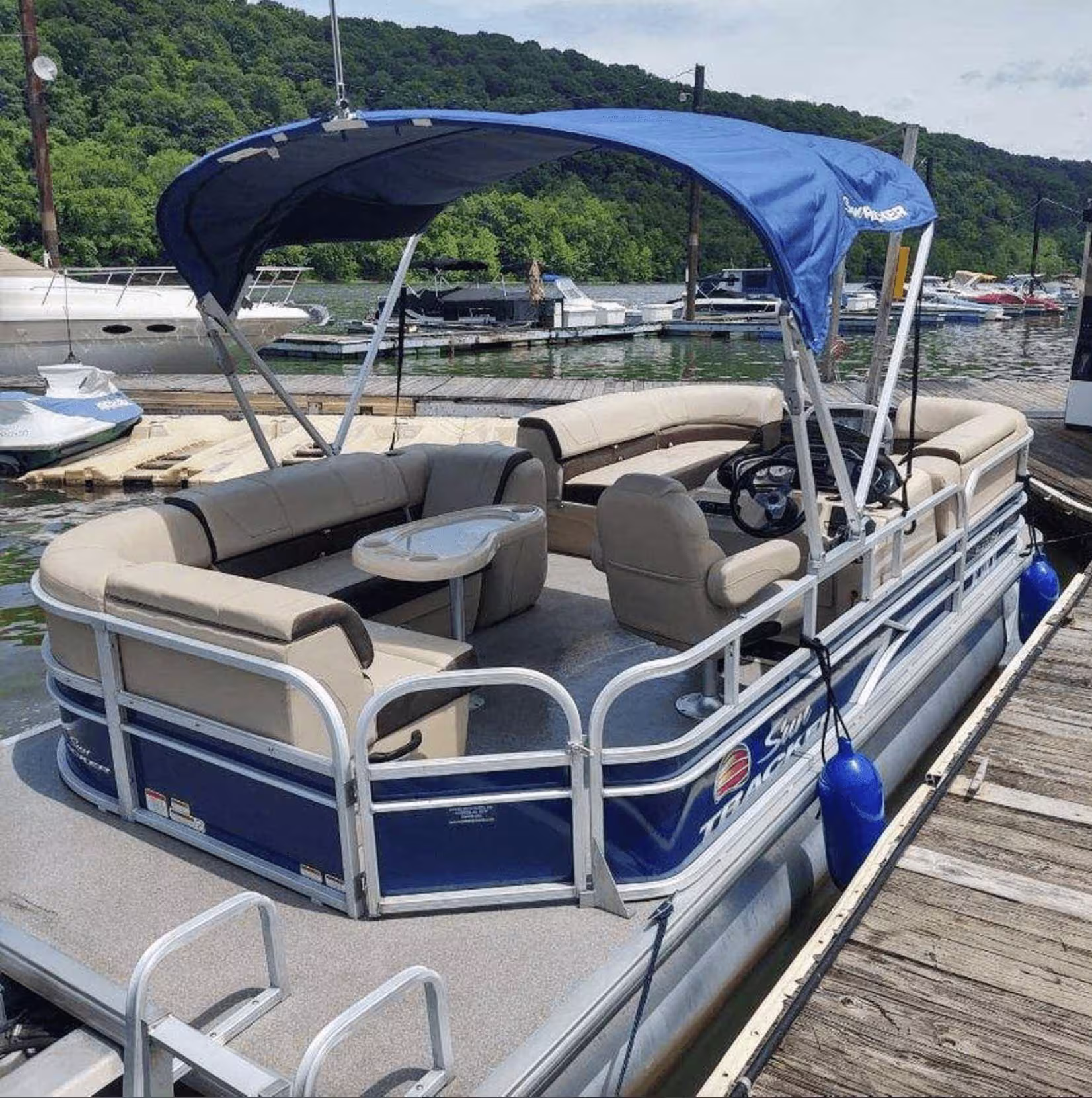 Pontoon boat with beige seating and a blue canopy docked at a marina