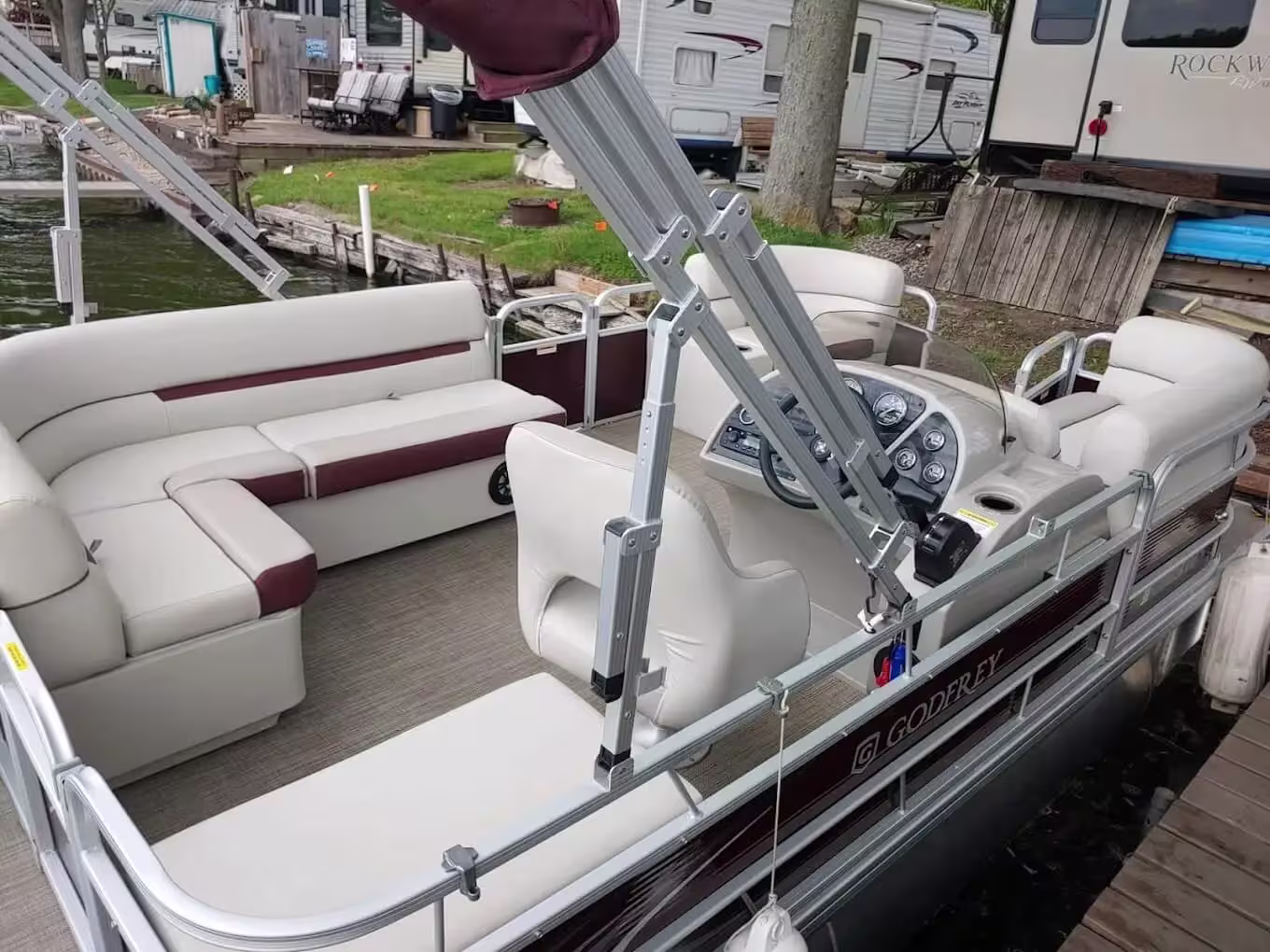 Pontoon boat with white and burgundy seating docked beside a waterfront campsite