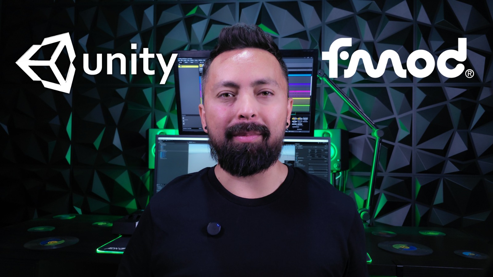 Composer Amadeus Herrera with beard standing in front of two computer monitors in a studio with Unity and FMOD logos on the background.