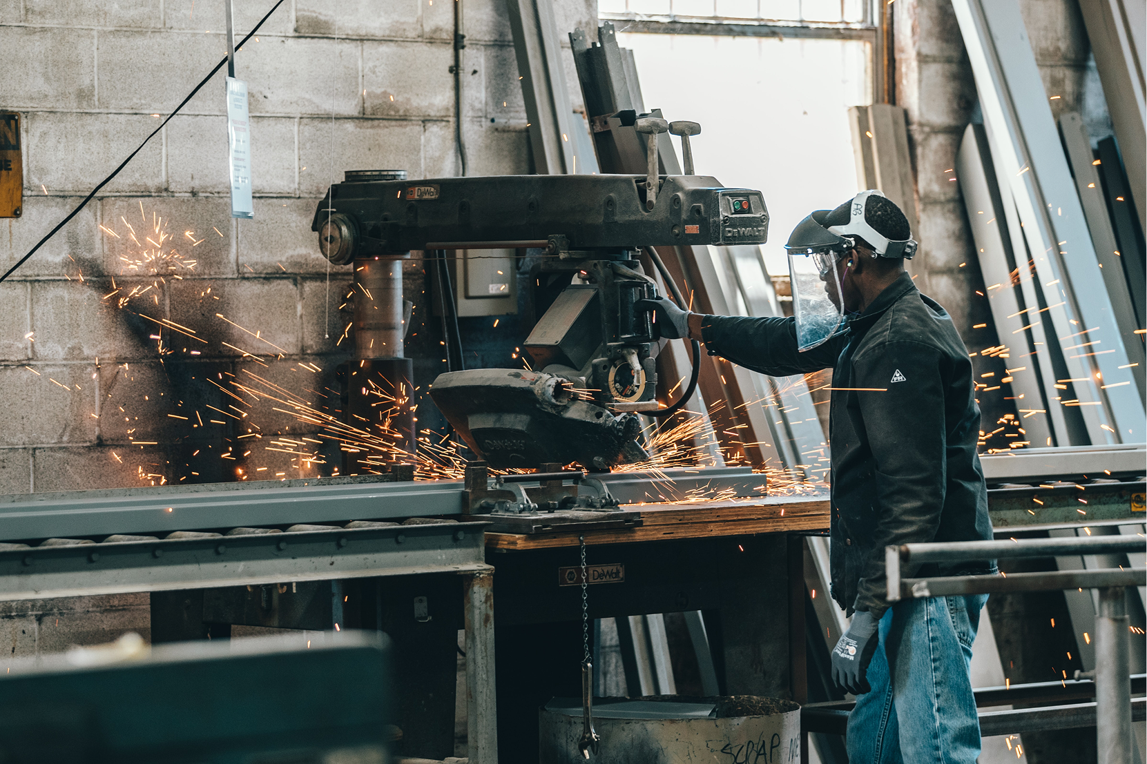 Worker wearing protective gear operating a metal cutting machine with sparks flying in an industrial workshop.