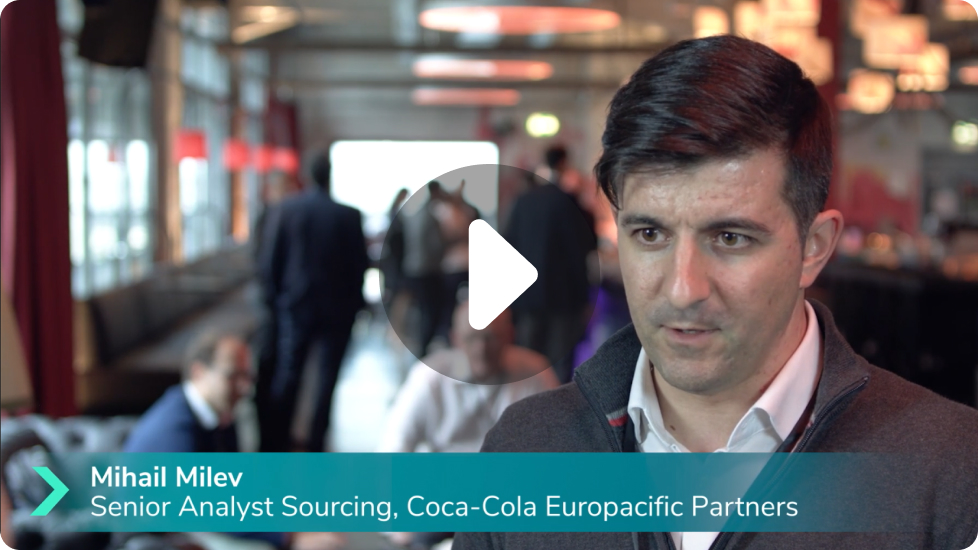Mihail Milev, Senior Analyst Sourcing at Coca-Cola Europacific Partners, speaking in a professional indoor setting with people in the blurred background.