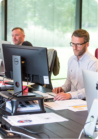 Two men working at desks with computers in a modern office with large windows.