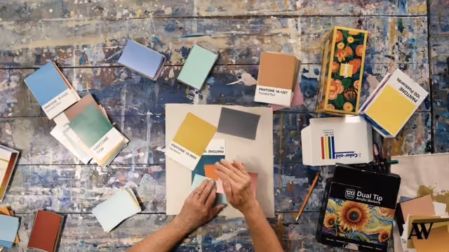 Hands arranging Pantone color swatches on a worn paint-splattered wooden surface.