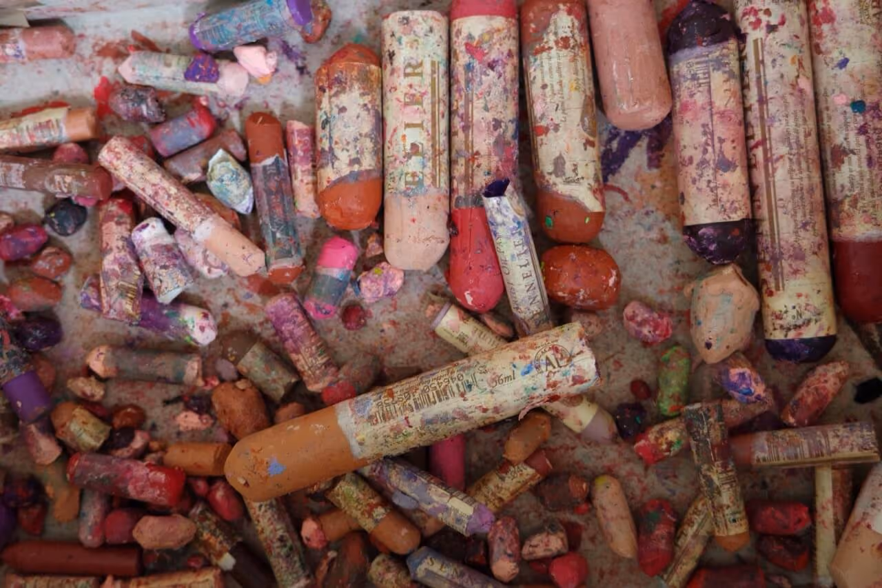 Close-up of worn oil pastel sticks scattered on a surface with various colors and labels visible.