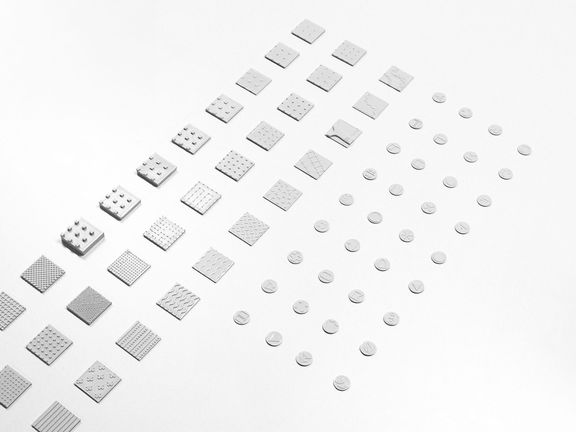 Rows of small, white textured square and circular samples with various raised patterns arranged diagonally on a white surface.