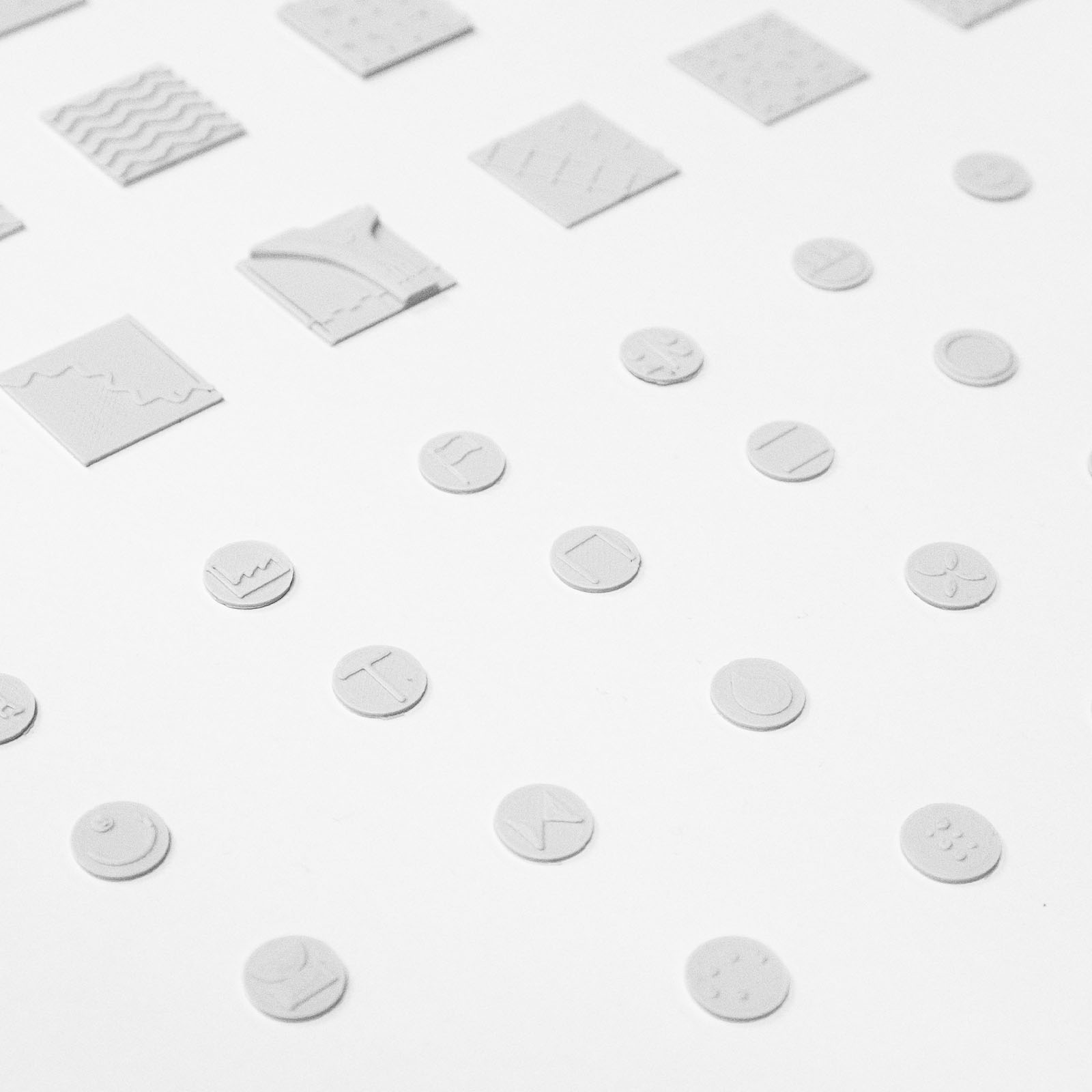 Close-up of white circular and square tokens arranged on a white surface with various abstract embossed designs.