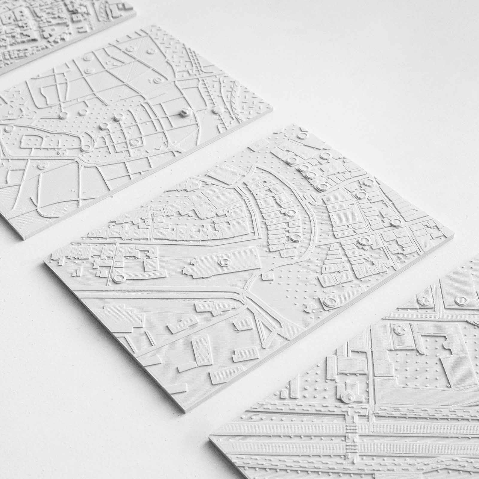 Three white embossed map tiles with detailed streets and building outlines laid out on a white surface.