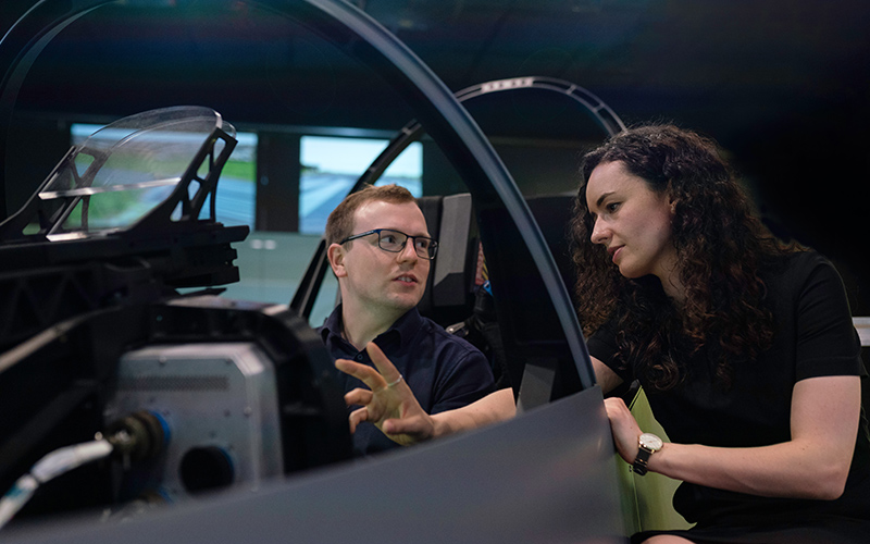 Female aerospace engineer talks with colleague in flight simulator